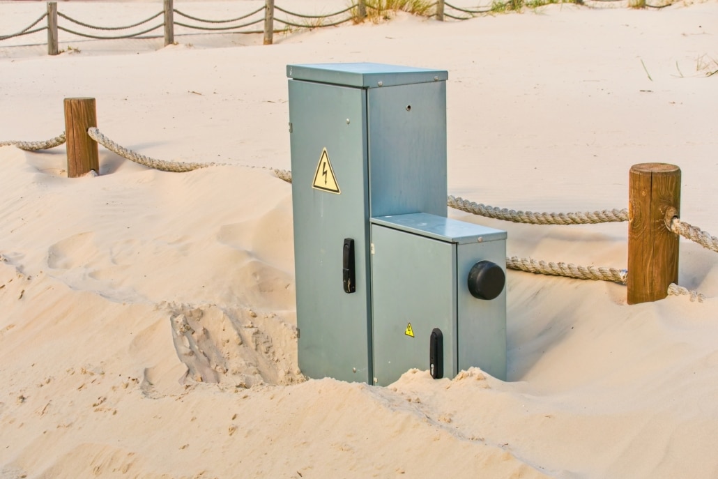 Zwei Schaltschränke unterschiedlicher Größe stehen allein in einer sandigen Landschaft.